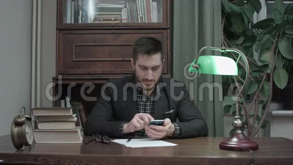 年轻的作家在他的办公桌上快乐地传递手机信息视频的预览图