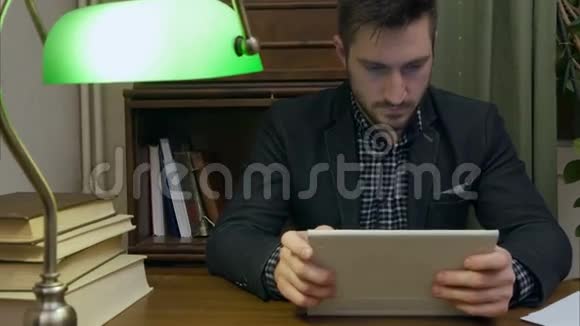 集中精力的年轻人坐在办公桌前拿着用数码平板电脑写的书视频的预览图