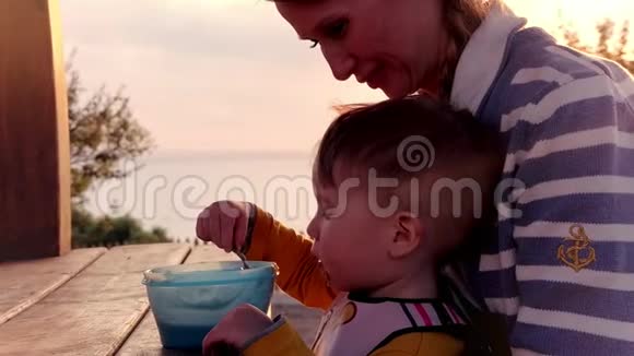 小男孩在餐桌上吃婴儿食品坐在妈妈的腿上吃着日落视频的预览图