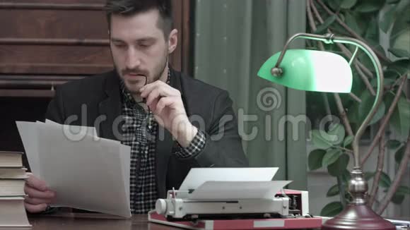 年轻的记者拿着打字机坐在书桌前看印刷文章视频的预览图