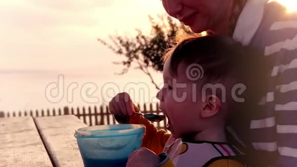 晚餐男孩吃婴儿食品坐在母亲腿上背景是明亮的阳光视频的预览图