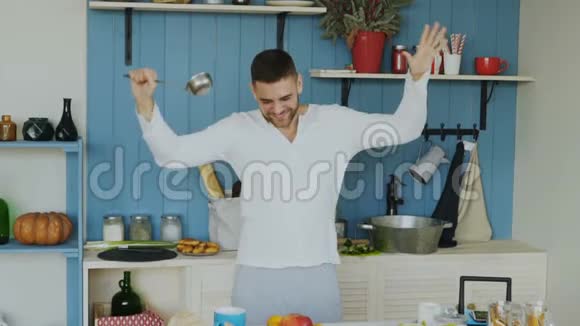在家厨房做饭时有魅力的年轻滑稽男子用勺子跳舞唱歌视频的预览图
