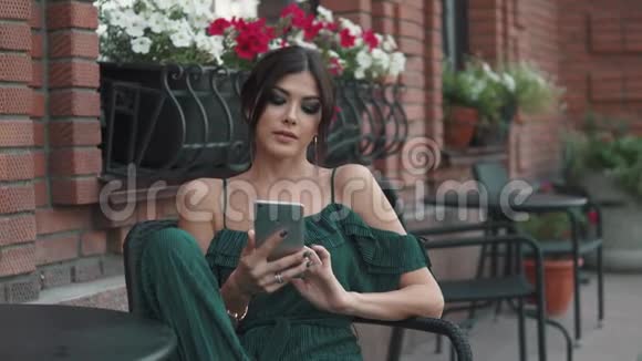 迷人的女孩用手机坐在古镇的户外咖啡馆里年轻迷人的女人正在打字视频的预览图