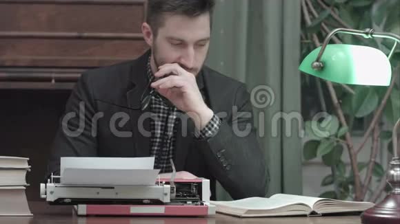 严肃的年轻人戴着眼镜坐在书桌前拿着打字机和看书视频的预览图