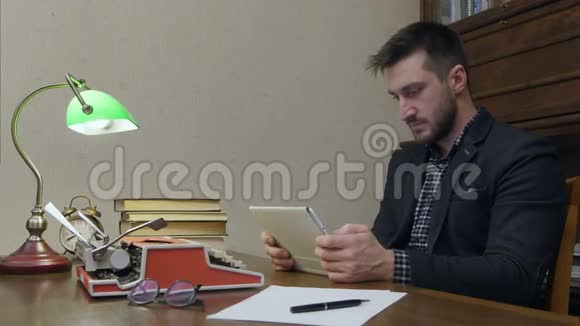 男性研究人员使用数字平板电脑坐在书桌前拿着书和打字机视频的预览图