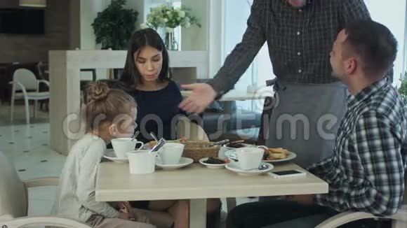 快乐的母亲父亲和小女孩吃晚饭请服务员用智能手机拍照视频的预览图