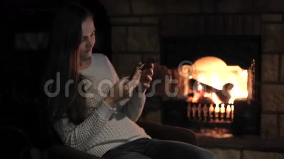 年轻女子坐着智能手机背景是壁炉视频的预览图