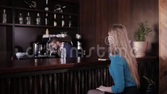 美丽的女孩坐在酒吧里等待鸡尾酒为可爱的酒保做准备视频的预览图