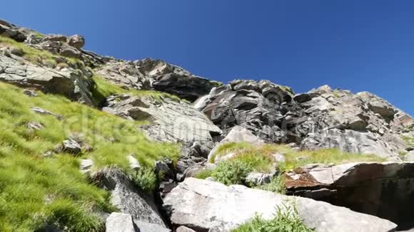 瀑布在田园诗般的无污染环境中流动夏天穿过阿尔卑斯山上的绿色草地和巨石慢动作z视频的预览图