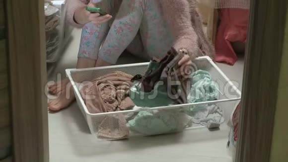 一个漂亮的女孩微笑着在更衣室里把衣服叠在篮子里把事情井井有条使用智能手机视频的预览图