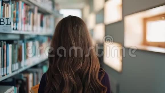 留着长发的女孩沿着图书馆的书架散步视频的预览图