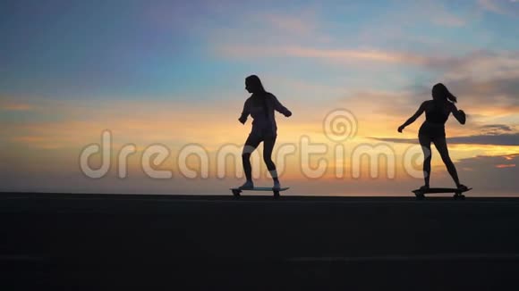 两个女孩在天空和阳光下的滑板轮廓视频的预览图