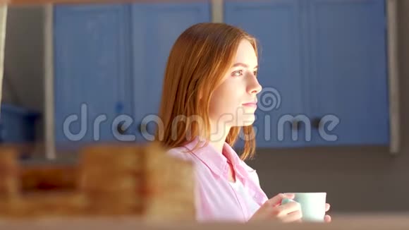 年轻漂亮的女人站在厨房里喝茶视频的预览图
