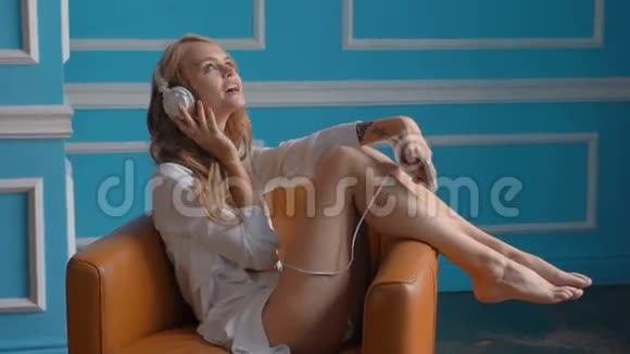 快乐的女孩坐在家里的扶手椅上听手机音乐视频的预览图
