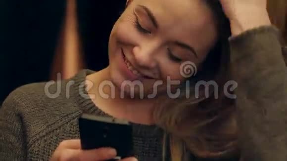 快乐的女人晚上在咖啡馆里用手机发短信微笑视频的预览图