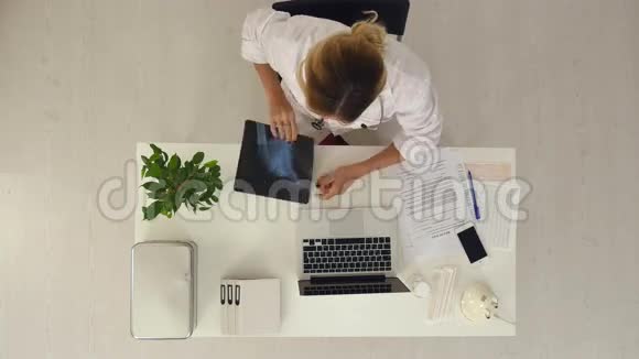年轻的女医生在办公室工作拿着X光检查结果用她的笔记本电脑视频的预览图