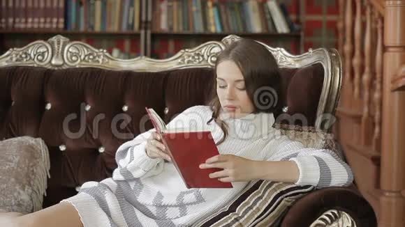 美丽的女人穿着白色套头衫躺在沙发上看书视频的预览图