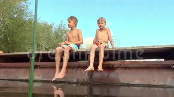 男孩们在湖边放松坐在码头边上摆动腿视频的预览图