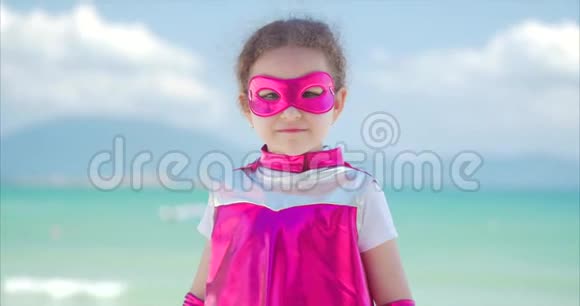 美丽的小女孩穿着超级英雄的服装穿着粉红色的斗篷和英雄的面具坐在飞机上视频的预览图