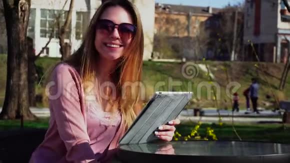 迷人的女孩在公园里用平板电脑工作戴着太阳镜休息视频的预览图