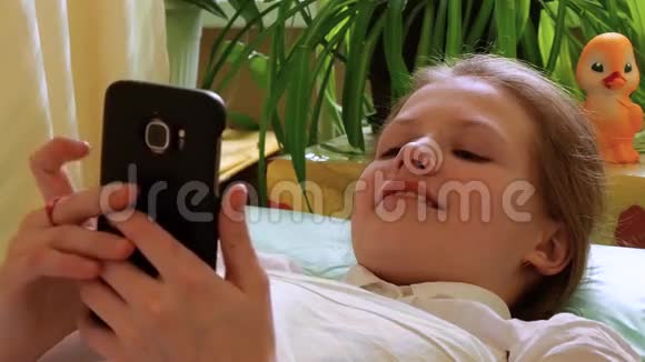 小女孩看着躺在医院沙发上的智能手机视频的预览图
