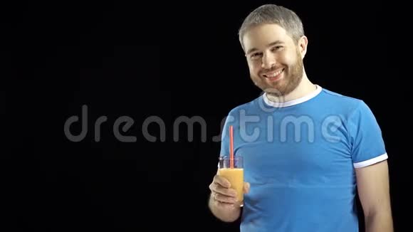穿着蓝色t恤的长着胡子的运动青年用吸管喝橙汁黑色背景4K视频视频的预览图
