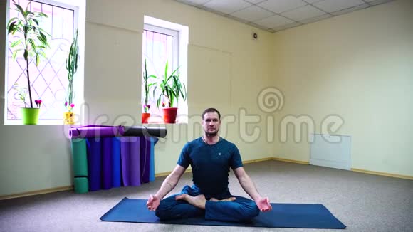 英俊的男人坐在地毯上在莲花的位置瑜伽和冥想视频的预览图