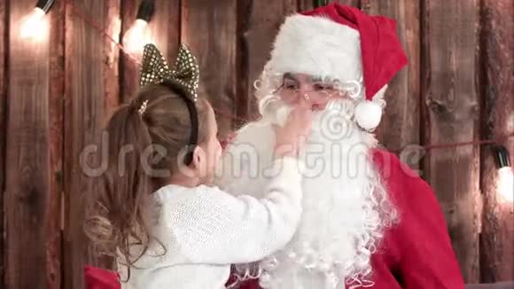 可爱的女孩玩圣诞老人的胡子坐他的腿视频的预览图