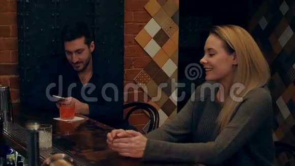男人用智能手机盯着身后年轻漂亮的女人而酒吧里的酒吧服务员则在准备鸡尾酒视频的预览图