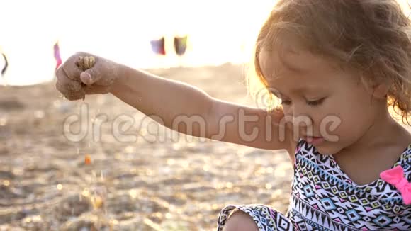 小女孩手里拿着沙子在海滩上让它再次掉下来视频的预览图