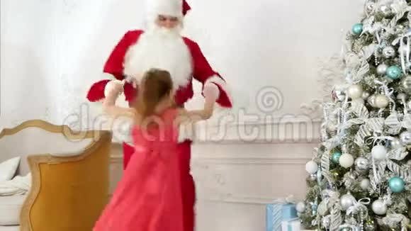 可爱的小女孩和圣诞老人在圣诞树旁边跳舞视频的预览图