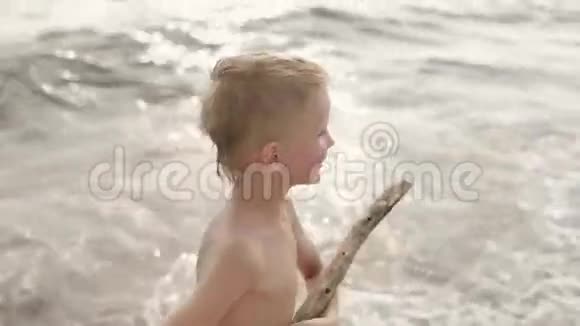欧洲外表的快乐男孩手里拿着一根棍子去海滩摄像机拍摄腿和脸视频的预览图