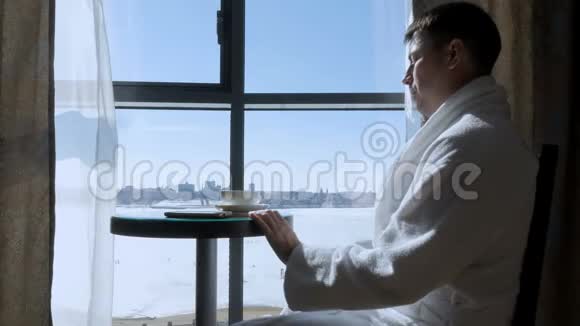 一个年轻人坐在窗边喝茶写短信视频的预览图