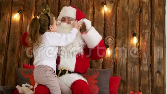 可爱的小女孩拉着圣诞老人胡子检查它是否真的坐在他的膝盖上视频的预览图