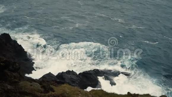 在阳光明媚的日子里近距离观看蓝色海洋的海岸波浪溅在黑色的岩石上视频的预览图