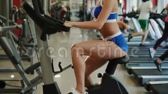 漂亮的女运动员在健身房里骑运动自行车锻炼4K视频的预览图