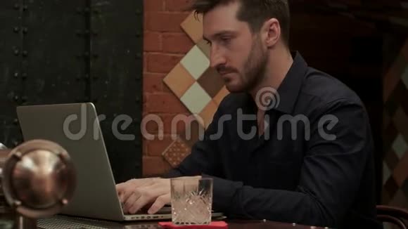一个英俊的商人在高档酒吧喝酒的时候在他的笔记本电脑上工作视频的预览图