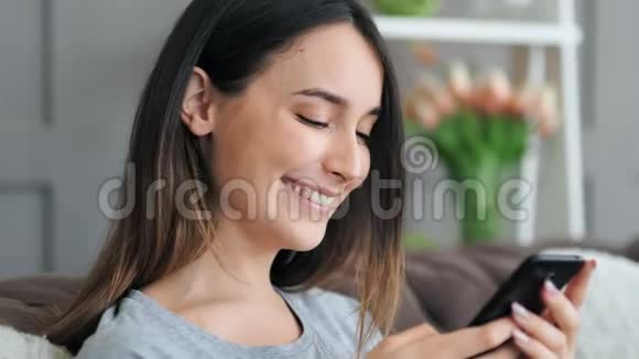 年轻漂亮的女人坐在沙发上用智能手机视频的预览图