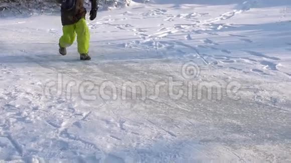 快乐的男孩跪在结冰的湖面上寒冷晴朗的冬日慢动作视频的预览图
