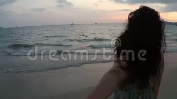 日落时分年轻女子牵着男性的手在沙滩上散步在海边快乐的微笑女孩的镜头点视频的预览图