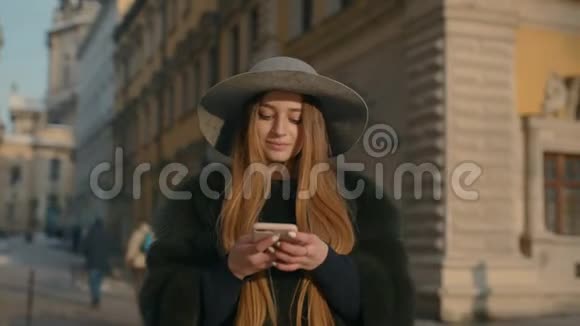 戴着灰色帽子的女人站在拥挤的城市街道上用手机发短信视频的预览图