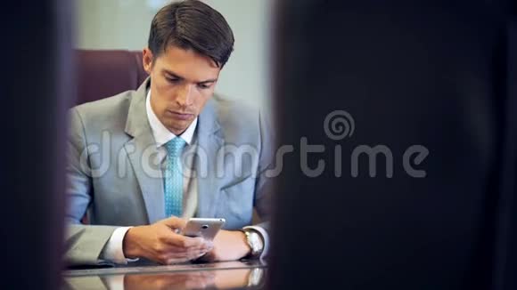 英俊的商人在办公室的智能手机上浏览互联网视频的预览图