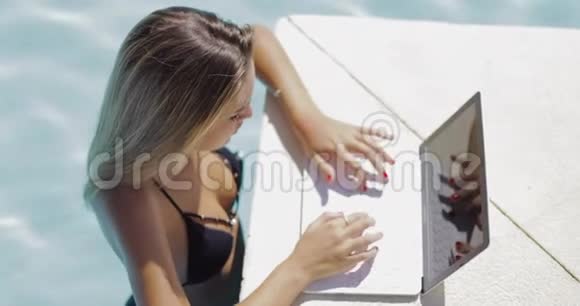 微笑的女人带着笔记本电脑在游泳池里放松视频的预览图