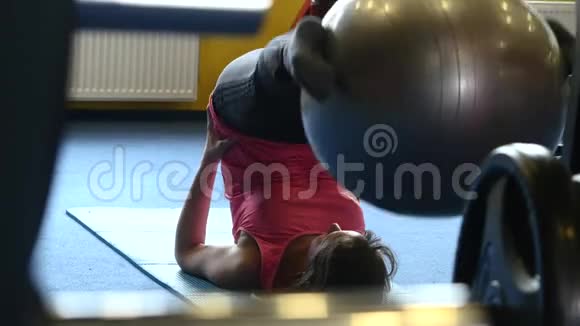 在健身房训练腹部肌肉的女人躺在你的瑜伽垫上把腿放在头上保持头部视频的预览图