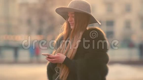 美丽的黑发女人戴着灰色帽子站在拥挤的城市街道上用她的电话视频的预览图