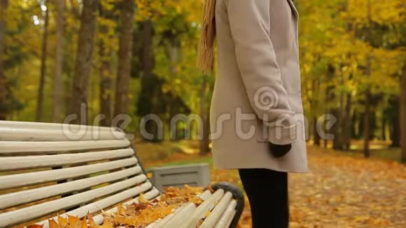 在秋天公园里一位优雅的年轻女子坐在长凳上感到冷视频的预览图