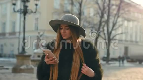 布鲁内特女士戴着灰色帽子站在拥挤的城市街道上用手机发短信视频的预览图