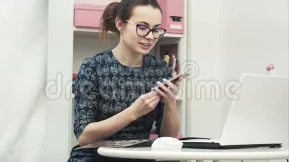 年轻有魅力的女时装设计师使用电脑笔记本电脑在制造办公室打手机视频的预览图