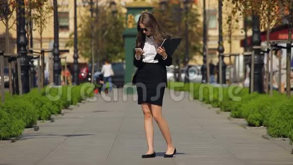 漂亮的女商人带着剪贴板在智能手机上说话等待着视频的预览图