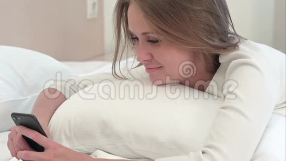 女人躺在床上用手机开心地笑着视频的预览图